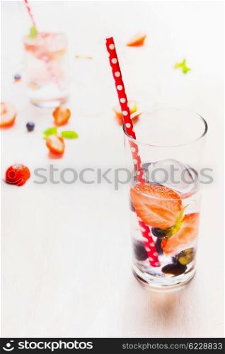 Glass with berries lemonade, ice cubes and red straw on white wooden background. Healthy vitamin drink.