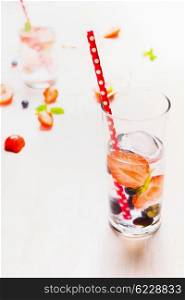 Glass with berries lemonade, ice cubes and red straw on white wooden background. Healthy vitamin drink.