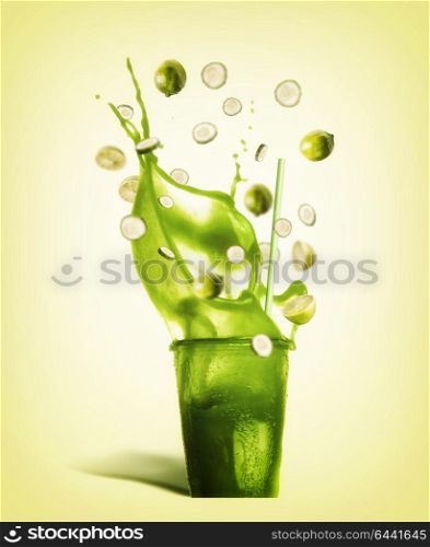 Glass with drinking straw and green splash summer beverage: smoothie, juice or lemonade with flying ingredients: lemon and cucumber slices on yellow background, front view