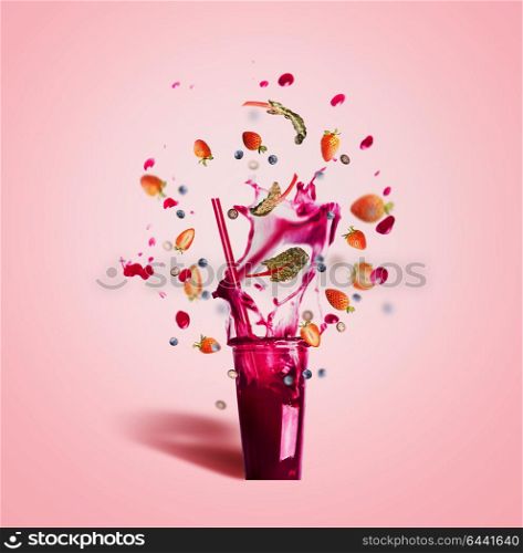 Glass with drinking straw and purple splash summer beverage: smoothie or juice with flying berries ingredients on pink background, front view