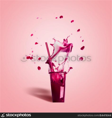 Glass with drinking straw and purple splash summer beverage: smoothie or juice on pink background, front view