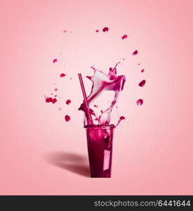 Glass with drinking straw and purple splash summer beverage: smoothie or juice on pink background, front view