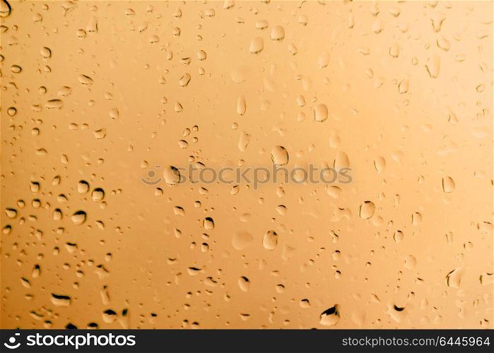 Glass with drops of rain water close up with orange color