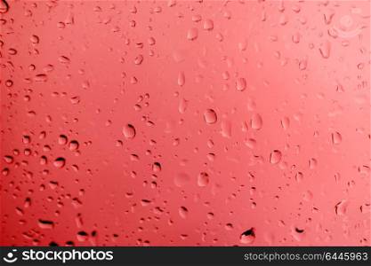 Glass with drops of rain water close up with red color