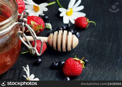 Glass with honey raspberry and flowers chamomiles on dark background. Wooden dipper . Selective focus .. Glass with honey raspberry and flowers chamomiles on dark background. Wooden dipper . Selective focus