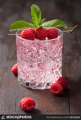 Glass with ice of summer pink lemonade cocktail with raspberries, mint and raw berries on wooden background. Macro