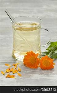 Glass with pot marigold tea with fresh flowers and leaves