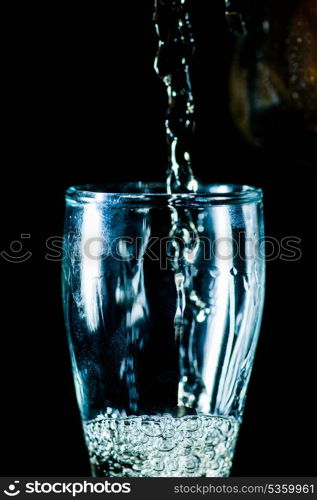glass with pouring drink on black