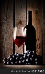 Glass with red wine bottle and grapes on a wooden background