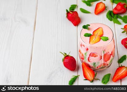 Glass with strawberry cocktail on a white wooden background. Strawberries and spruce tips scattered on the table, ingredients for making smoothies. Smoothie top view with copy space.
