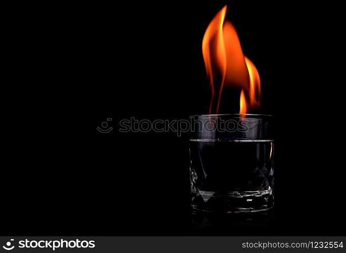 Glass with vodca and fire flame on black background