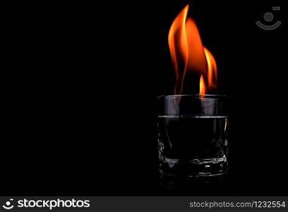 Glass with vodca and fire flame on black background