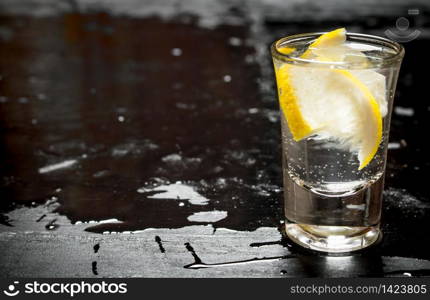 Glass with vodka and lemon. On a black wooden background.. Glass with vodka and lemon.