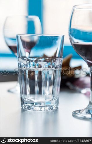 glass with water and wineglasses with red on blue window background