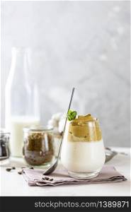 Glass with water drops of iced frothy drink Dalgona Coffee, trend korean drink latte espresso with coffee. White wooden table surface.