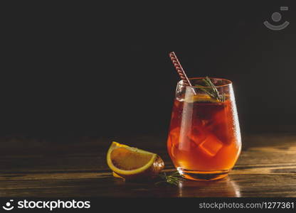 Glass with water drops of Italian aperol spritz cocktail with orange slices, ice and minton dark wooden table with amazing back light. Milano spritzer alcoholic cocktail with red bitter, dry white wine.