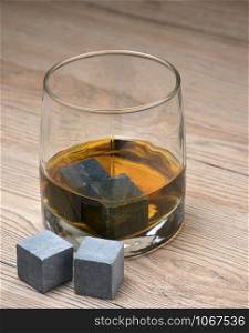 Glass with whiskey and whiskey stones on wooden background