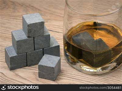 Glass with whiskey and whiskey stones on wooden background.