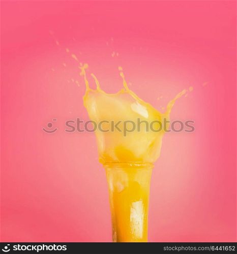 Glass with yellow splash summer beverage: smoothie or juice at pink background, front view