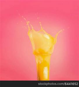 Glass with yellow splash summer beverage: smoothie or juice at pink background, front view