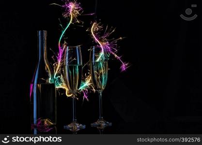 Glasses and a bottle of champagne in the light of Bengal lights. Black background. The concept of the celebration of the wedding and the new year. Copy space.. Glasses and a bottle of champagne in the light of Bengal lights