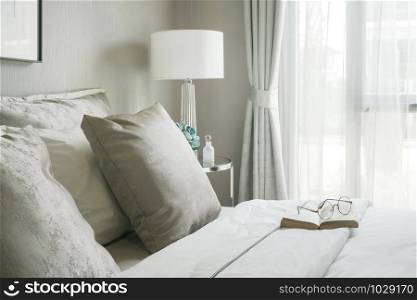 Glasses and book on comfortable bed in modern interior bedroom
