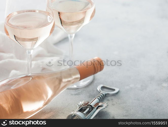 Glasses and bottle of rose pink wine with steel corkscrew on light table background.