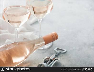 Glasses and bottle of rose pink wine with steel corkscrew on light table background.