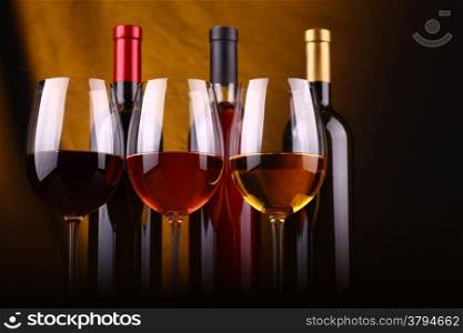 Glasses and bottles of red, rose and white wine over a draped background lit yellow