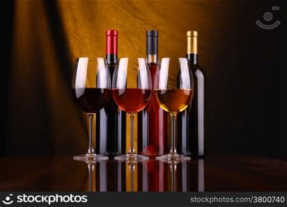 Glasses and bottles of red, rose and white wine over a draped background lit yellow