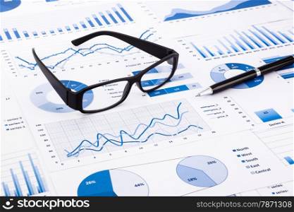 glasses and pen on blue charts, graphs, data and document background for financial and business concepts