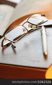 Glasses and the pen lay on the old book