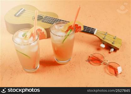 glasses citrus juice with ice cubes sunglasses ukulele orange textured backdrop