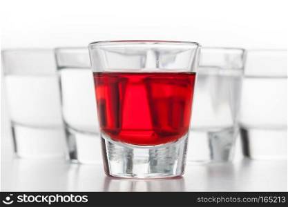 Glasses of alcohol. One red flavoured, the others clean vodka. White background.. Glasses of alcohol. One red flavoured, the others clean vodka.