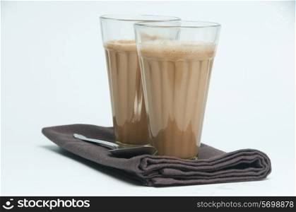 Glasses of chai and spoon kept on a table napkin isolated over white background