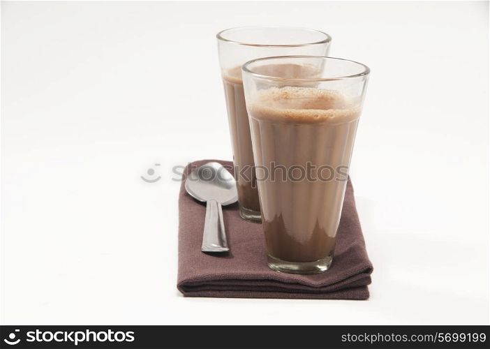 Glasses of chai and steel spoon kept on table napkin isolated over white background