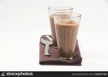 Glasses of chai and steel spoon kept on table napkin isolated over white background
