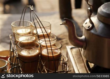 Glasses of chai kept in grid tray with kettle on stove