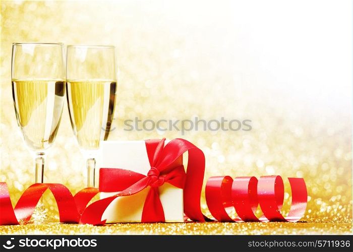 Glasses of champagne and box with gift on golden background