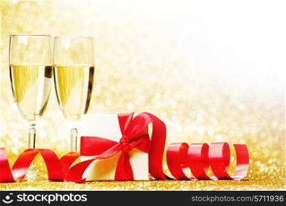 Glasses of champagne and box with gift on golden background