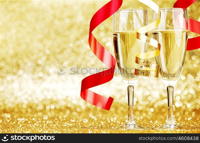 Glasses of champagne and red ribbons on golden background