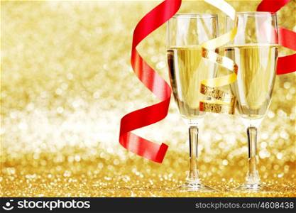 Glasses of champagne and red ribbons on golden background