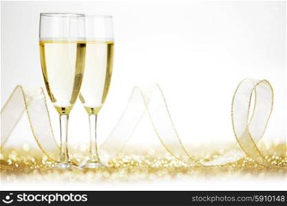 Glasses of champagne and ribbon on golden glitters isolated on white