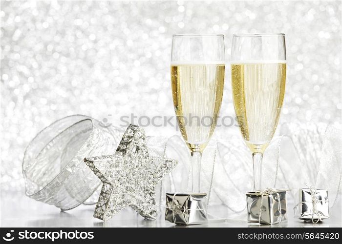 Glasses of champagne and silver gifts on glitter background