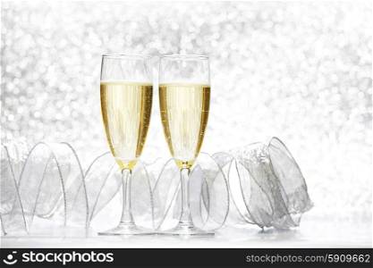 Glasses of champagne and silver ribbons on glitter background