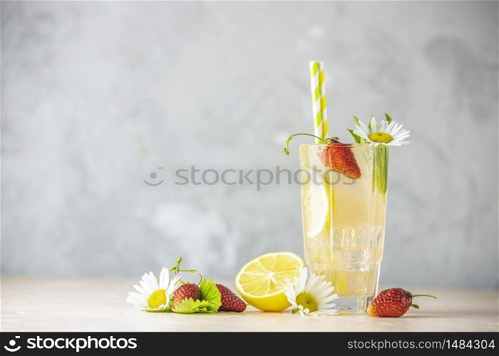 Glasses of cold icy refreshing drink with lemon and strawberry served on light pink table. Fresh cocktail drinks with ice fruit, herb and chamomile decoration.
