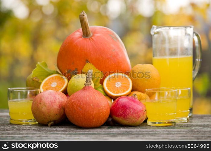 glasses of juice and lots of autumn fruits on wooden table, outdoor