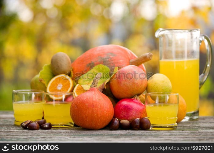 glasses of juice and lots of autumn fruits on wooden table, outdoor