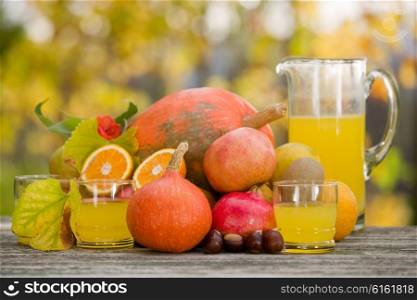 glasses of juice and lots of autumn fruits on wooden table, outdoor