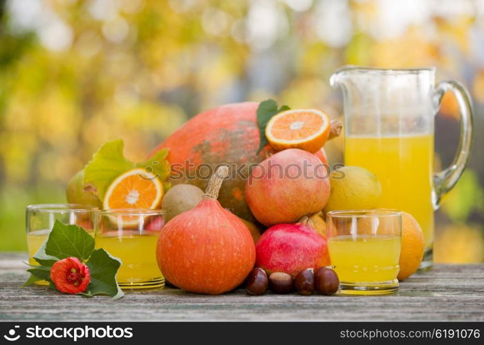 glasses of juice and lots of autumn fruits on wooden table, outdoor